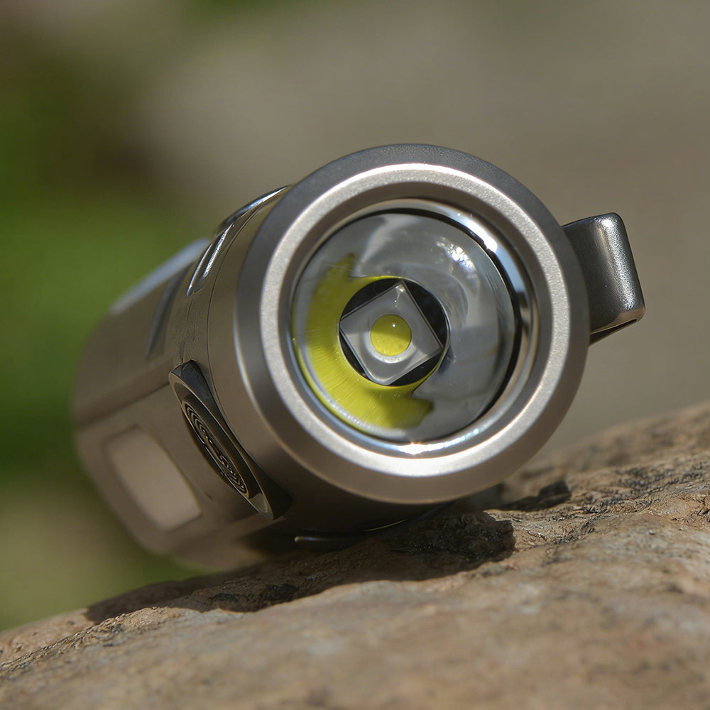 Close-up of a titanium flashlight on a rock with a blurred natural background