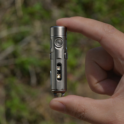 Hand holding a small metallic device against a blurred natural background